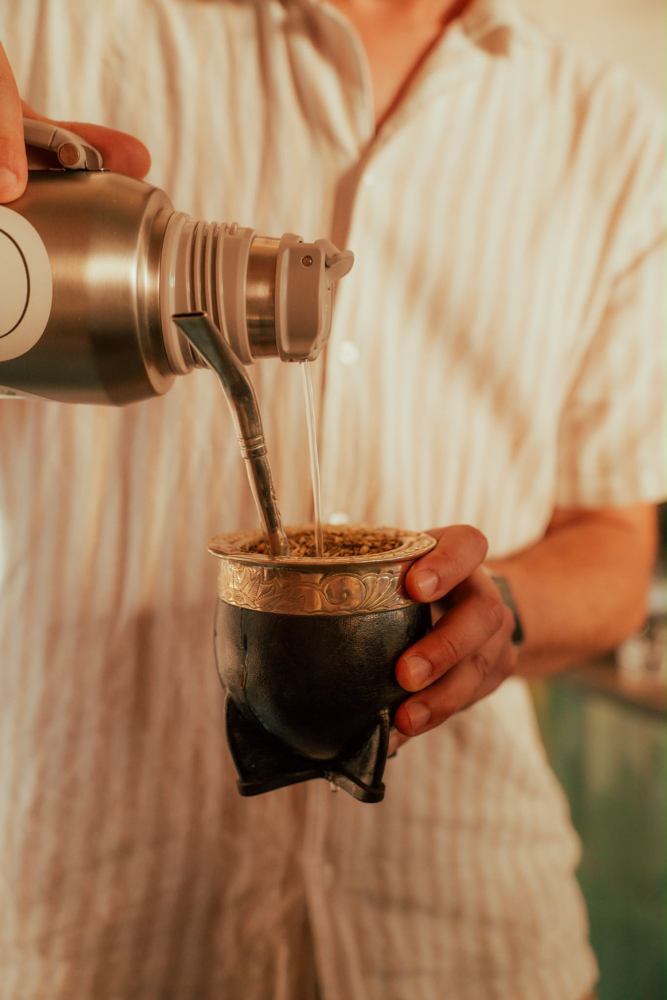 Pouring water from a thermos over yerba mate in a traditional gourd vessel